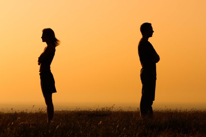 Silhouetted couple standing apart in a field at sunset, symbolizing emotional distance and relationship challenges